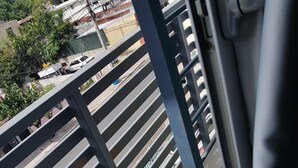 A metal railing with horizontal bars, a concrete floor, and a view of a street with buildings and parked cars. - Céntrico Próximo Clínica Unión Médica (Santiago de los Caballeros)