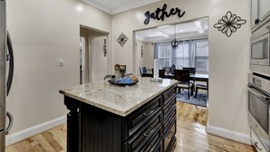 A kitchen with a granite island, black cabinetry, and a 'Gather' sign on the wall. - Unique Historical Home (Birmingham)