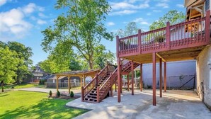 A covered patio area with a wooden staircase leading to a deck, surrounded by a grassy lawn and trees. - Unique Historical Home (Birmingham)