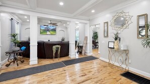 A spacious living room with hardwood flooring, a dark-colored sofa, a television mounted on the wall, and a decorative mirror. - Unique Historical Home (Birmingham)