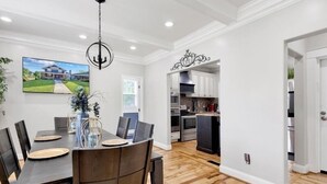 A dining area with a wooden table and chairs, a chandelier, and a painting of a house on the wall. - Unique Historical Home (Birmingham)