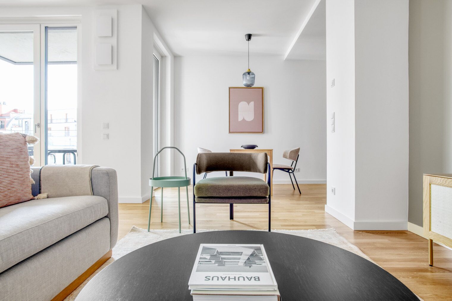Ein modernes Wohnzimmer mit einer Couch, Sesseln, einem Couchtisch mit einer Zeitschrift und einer Pendelleuchte.