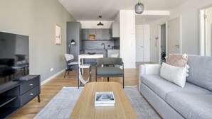 A modern living room with a sofa, coffee table, and TV. There is a kitchen area with cabinets and a dining table. - Gorgeous Mitte 1BR with Apple Store in building, by Blueground (Berlin)