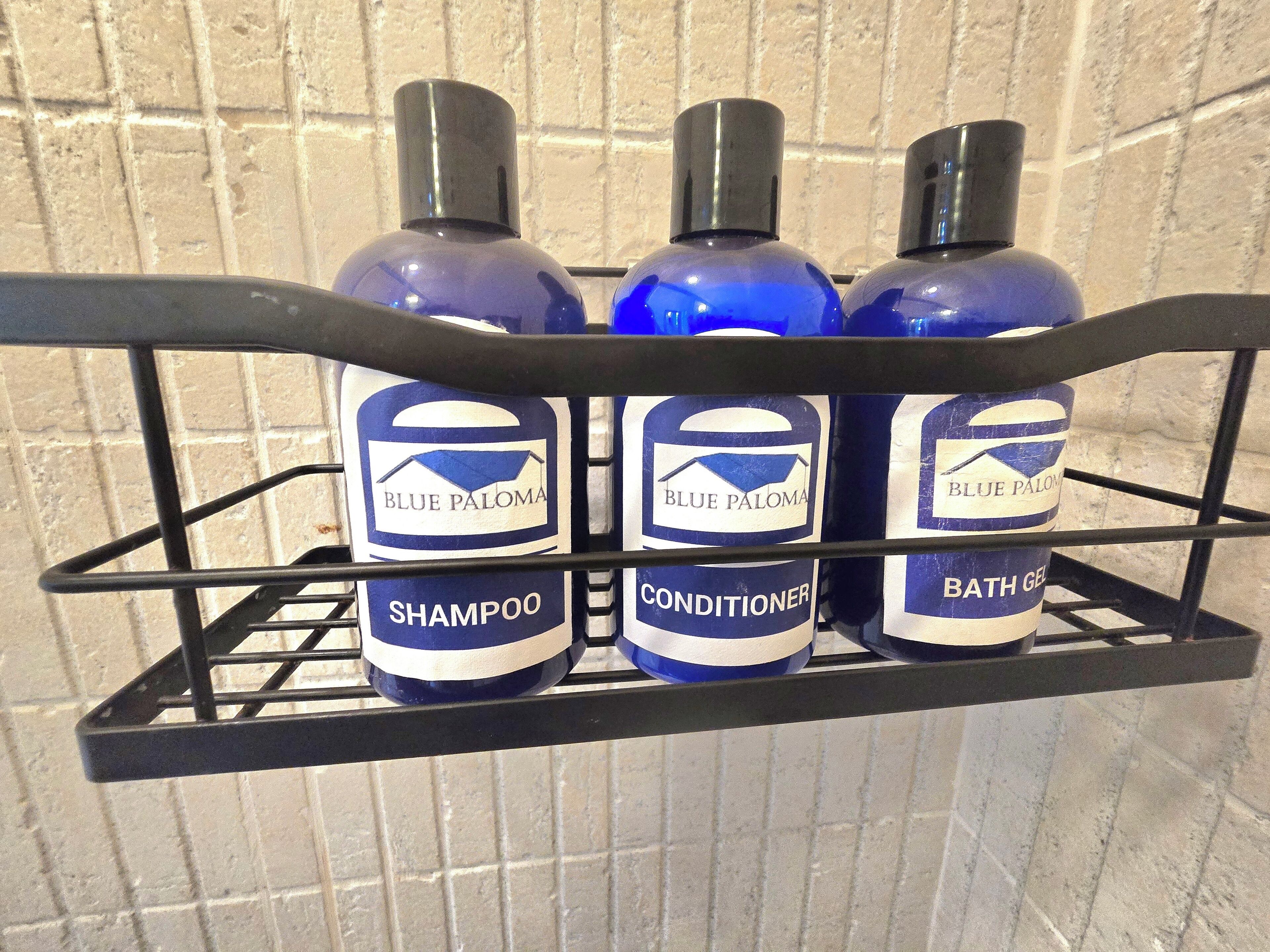 A metal rack holding three bottles of Blue Paloma products: shampoo, conditioner, and bath gel.