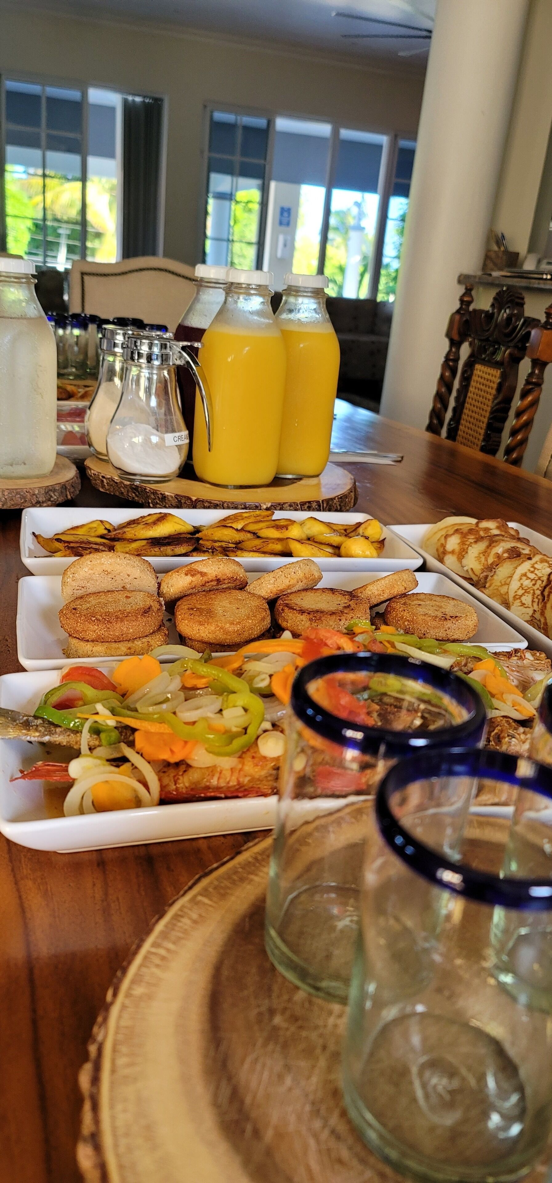Un buffet de petit-déjeuner proposant divers plats, notamment du pain, des viennoiseries et un plat de poisson, ainsi que deux carafes de jus d’orange.