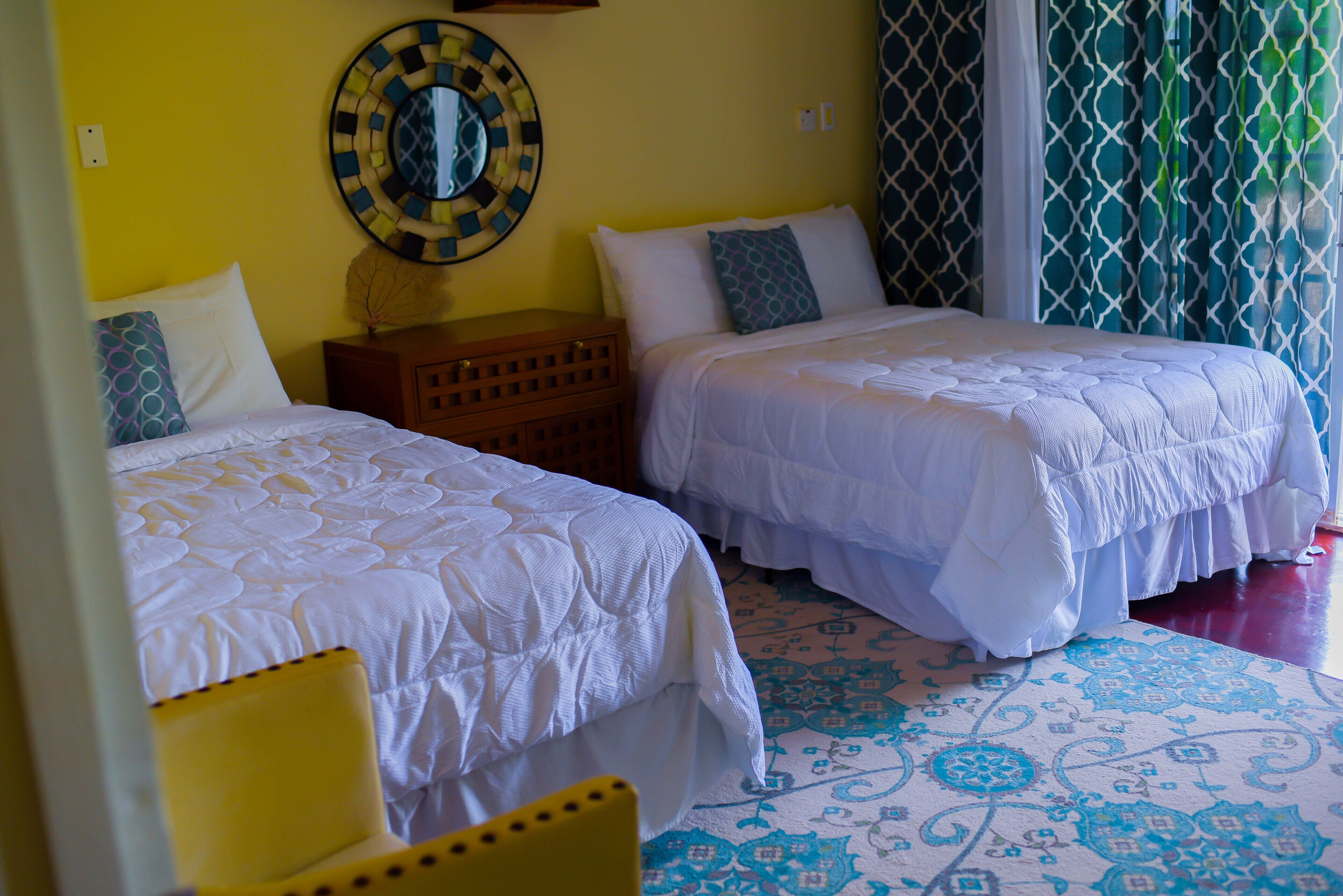 A room with two beds, a wooden nightstand, a yellow chair, and a patterned floor.