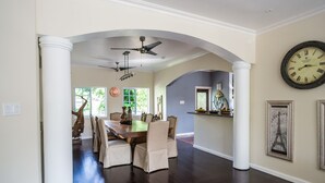 A dining area with a wooden table and chairs, a ceiling fan, and a large wall clock. - Blue Paloma Bed & Breakfast (Lucea)