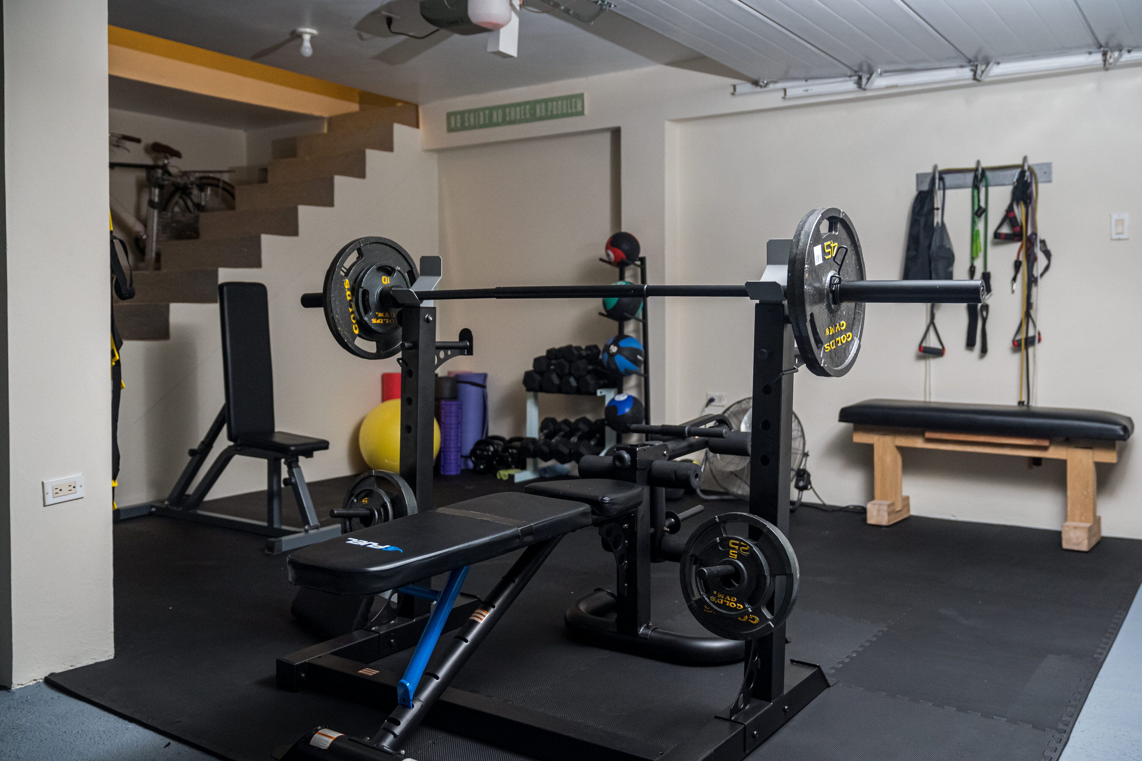 A home gym with a bench press, squat rack, and various weights.