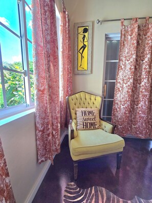 A room with a yellow armchair, a framed artwork, and red patterned curtains.