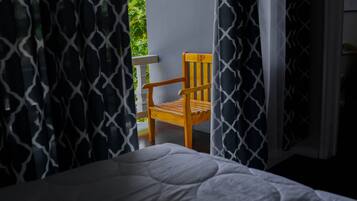 Una cama con colcha blanca, una silla de madera con reposacabezas y cortinas estampadas.