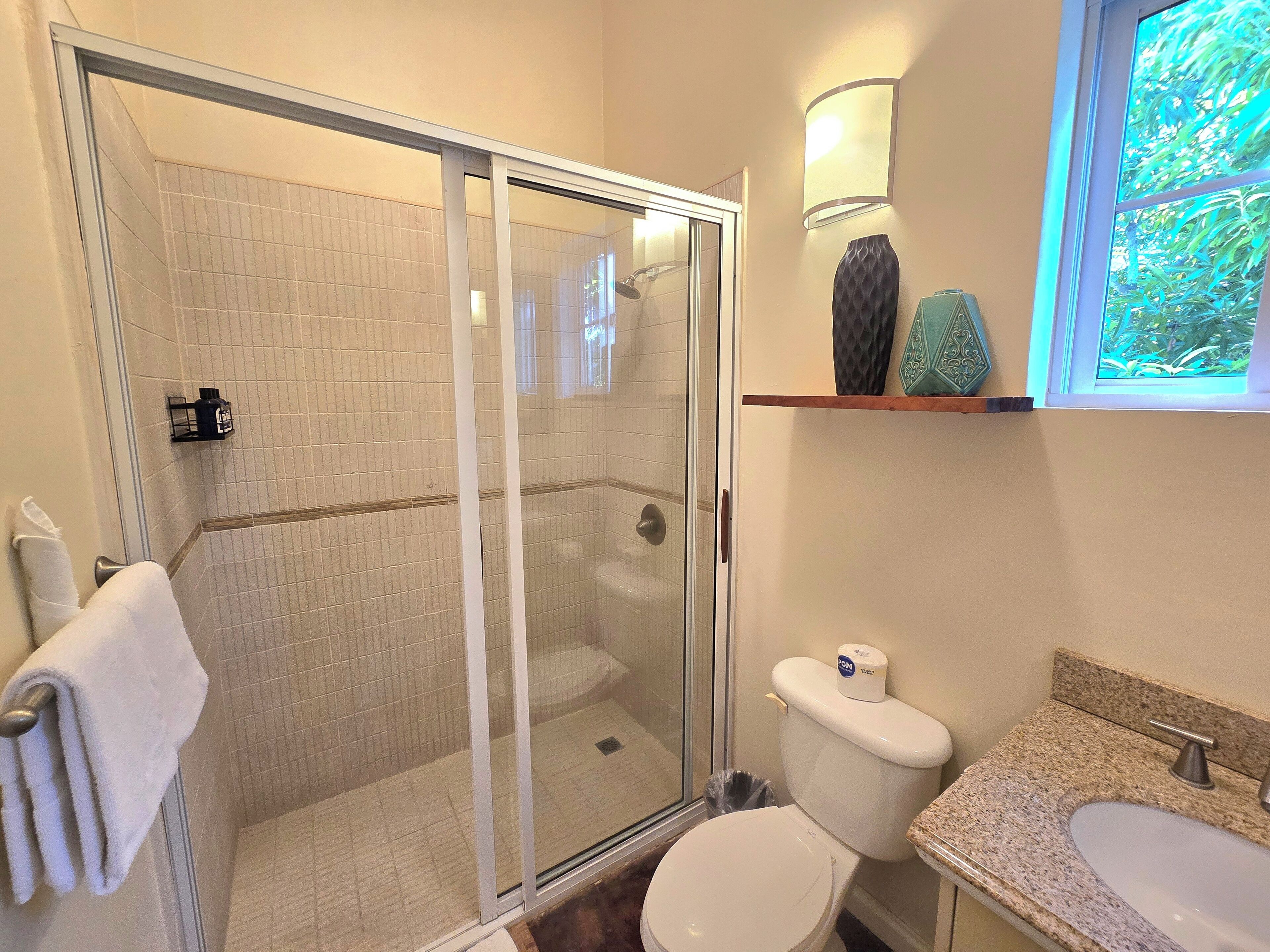 Bagno con doccia vetrata, un water, un lavandino e una finestra con vista sul verde.