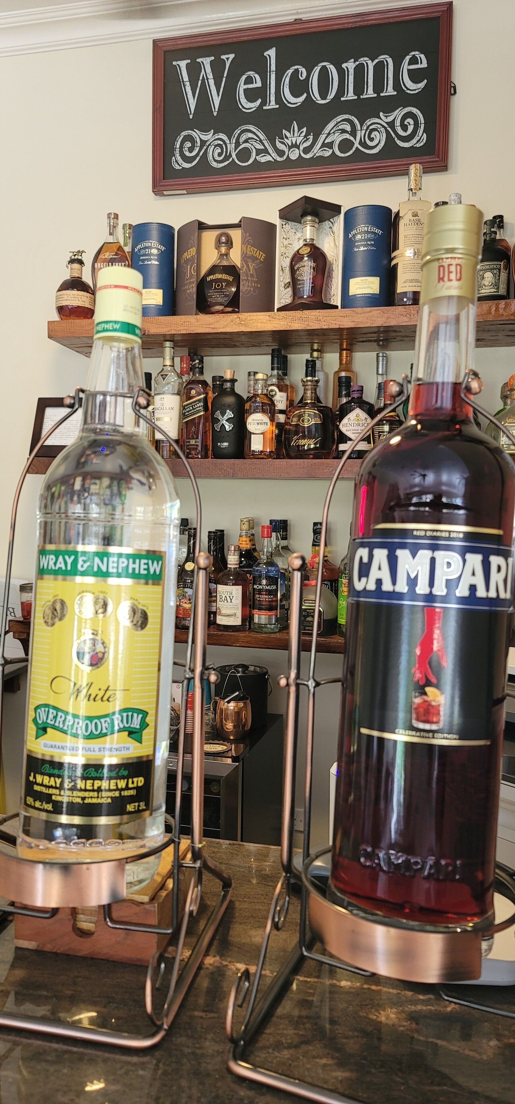 Duas garrafas de rum em um balcão de bar, com uma placa de 'Welcome' acima.