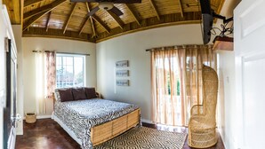 A bedroom with a bed, a ceiling fan, a television, and a wicker chair. - Blue Paloma Bed & Breakfast (Lucea)
