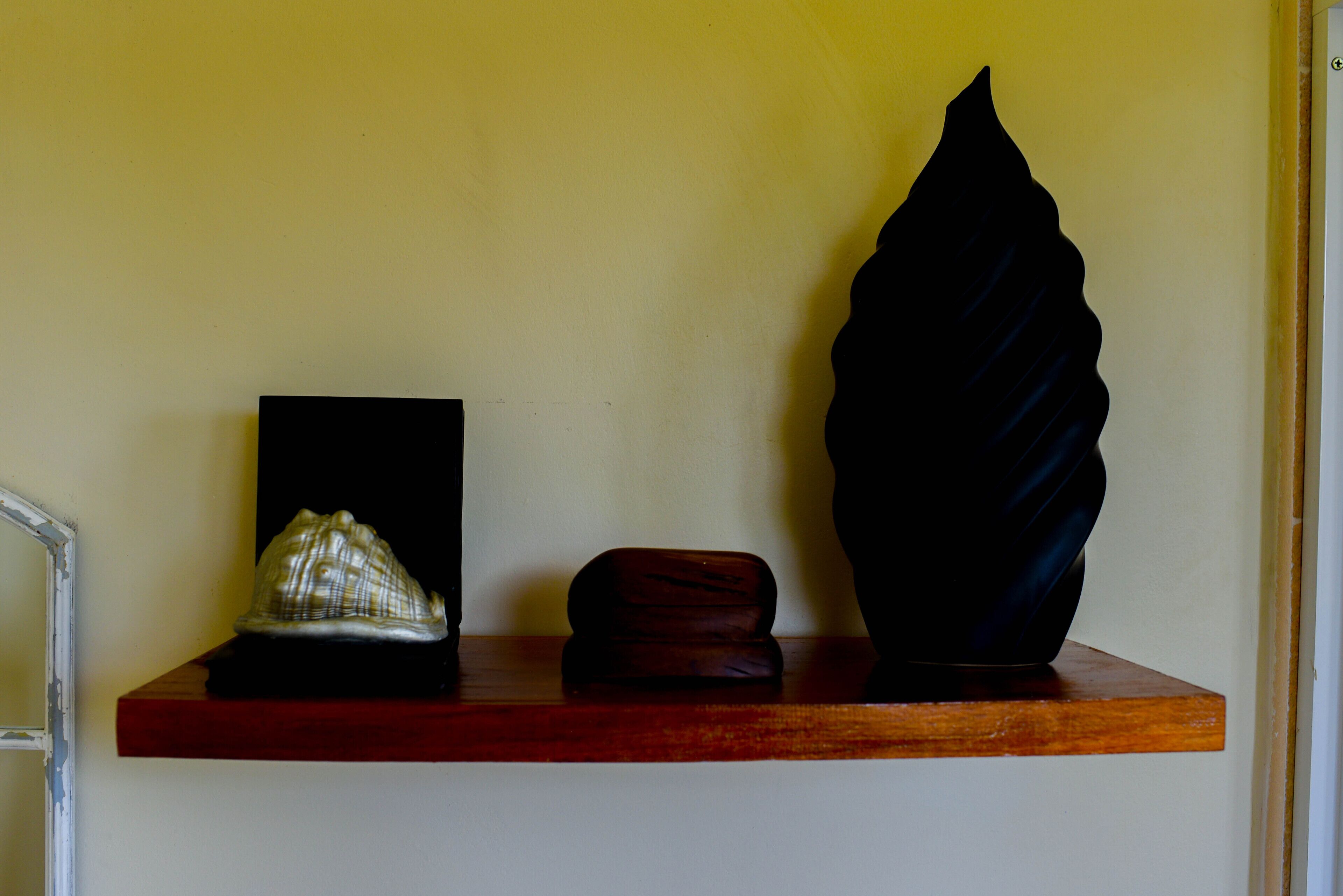 Una repisa con tres objetos decorativos: una concha, una caja de madera y un florero negro.