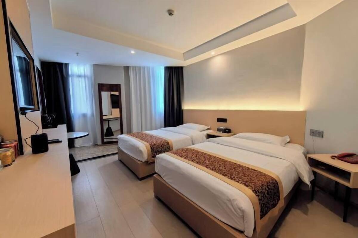Ein Hotelzimmer mit zwei Betten, einem Schreibtisch, einem Stuhl, einem Fernseher und einem Spiegel.