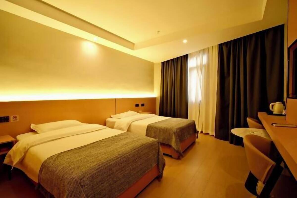 Ein Hotelzimmer mit zwei Betten, einem Schreibtisch, einem Stuhl und einem großen Fenster mit Vorhängen.