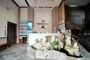 Un área de recepción con una fuente de piedra en forma de cascada, un mostrador de recepción y una escalera que conduce a un nivel superior.
