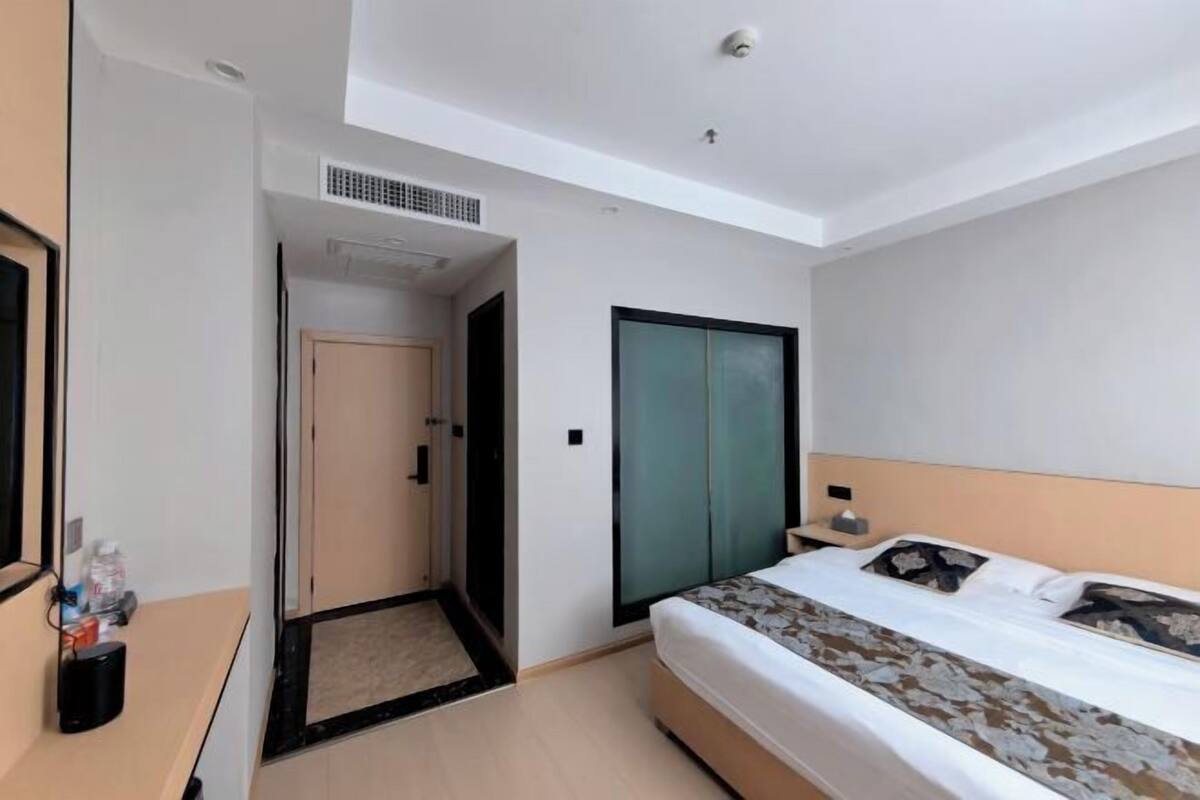 Ein Hotelzimmer mit einem Bett, einem Kleiderschrank, einem Schreibtisch mit Lampe und einer Tür zu einem weiteren Raum.