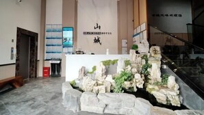 A reception area with a stone waterfall feature, a reception desk, and a staircase. - Zhijin Shancheng Hotel (Zhijin)