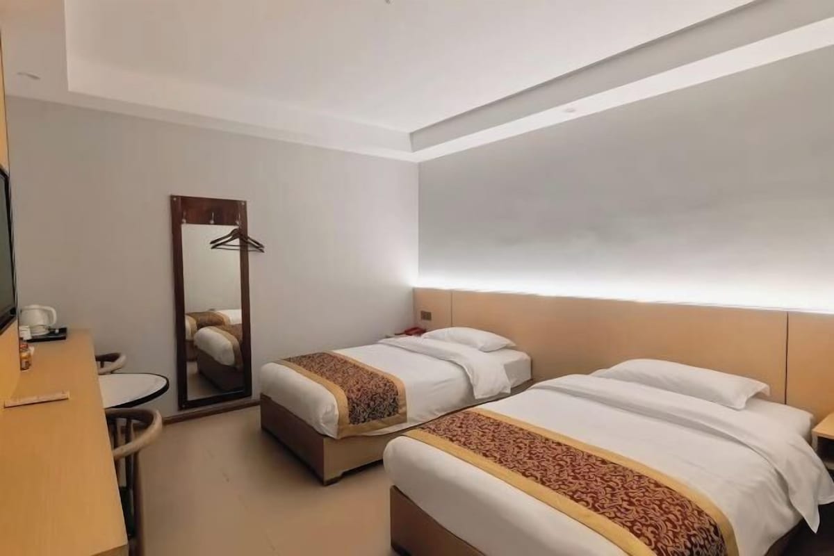 Habitación de hotel con dos camas, un escritorio, una silla, un espejo y un perchero.