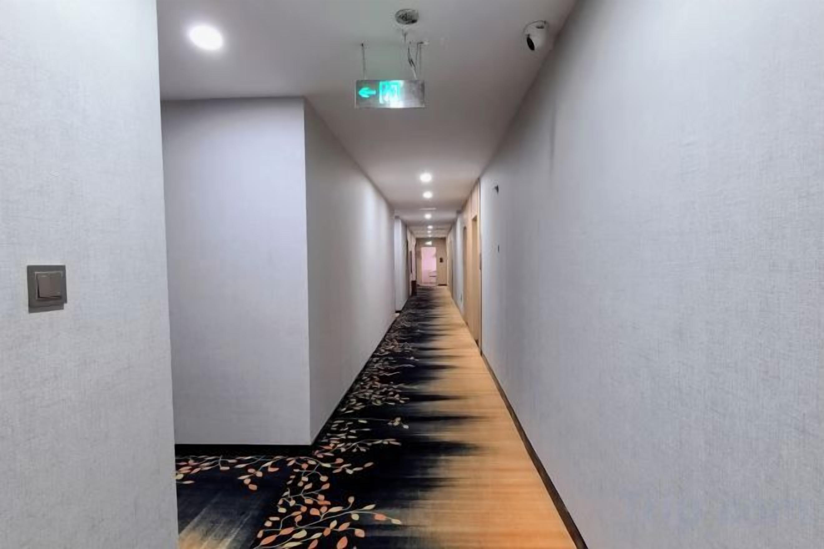 Un long couloir étroit, doté d’un sol recouvert de moquette et d’un projecteur au plafond.