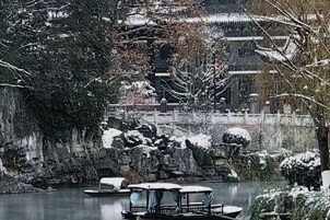 Un edificio tradicional con un puente, un estanque con barcos y árboles cubiertos de nieve.