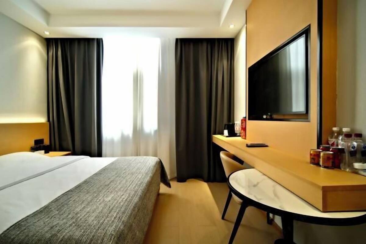 Ein Hotelzimmer mit Bett, Schreibtisch, Stuhl, Fernseher und einem Fenster mit Vorhängen.