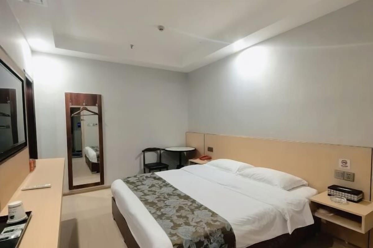 Una habitación de hotel con cama, mesita de noche, espejo, escritorio y silla.