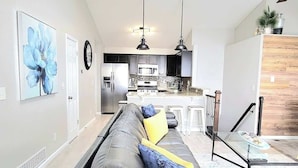 A modern living room with a sofa, a dining area, kitchen, and a staircase leading to an upper level. - $0Fees-6bed/6bath-Easy Red Rocks/Downtown/OldeTown (Arvada)