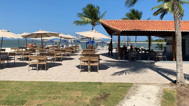 An outdoor seating area with tables and chairs, umbrellas, and a view of the sea. - Catamaran Praia Chalés (Igarassu)