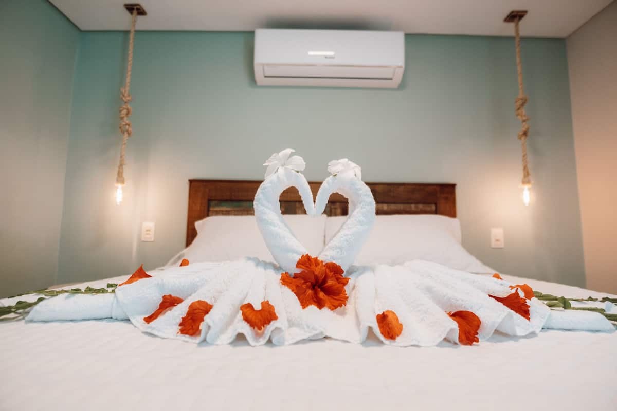 A neatly made bed with a heart-shaped towel arrangement and orange flowers.