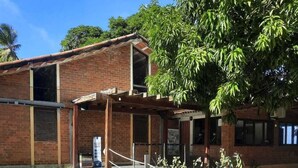 A brick building with a covered outdoor area and two large terracotta sculptures on the lawn. - Catamaran Praia Chalés (Igarassu)
