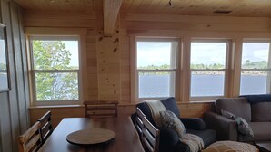 A wooden interior with a dining table, benches, a sofa, and large windows offering a view of a body of water. - Fabulous New Georgian Bay Cottage on the  water! (Byng Inlet)
