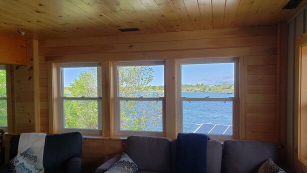 A cabin with a wooden interior, a couch with patterned cushions, and a view of a lake through large windows. - Fabulous New Georgian Bay Cottage on the  water! (Byng Inlet)
