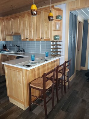 A kitchen with wooden cabinets, a central island with bar stools, pendant lights, and a tiled backsplash.