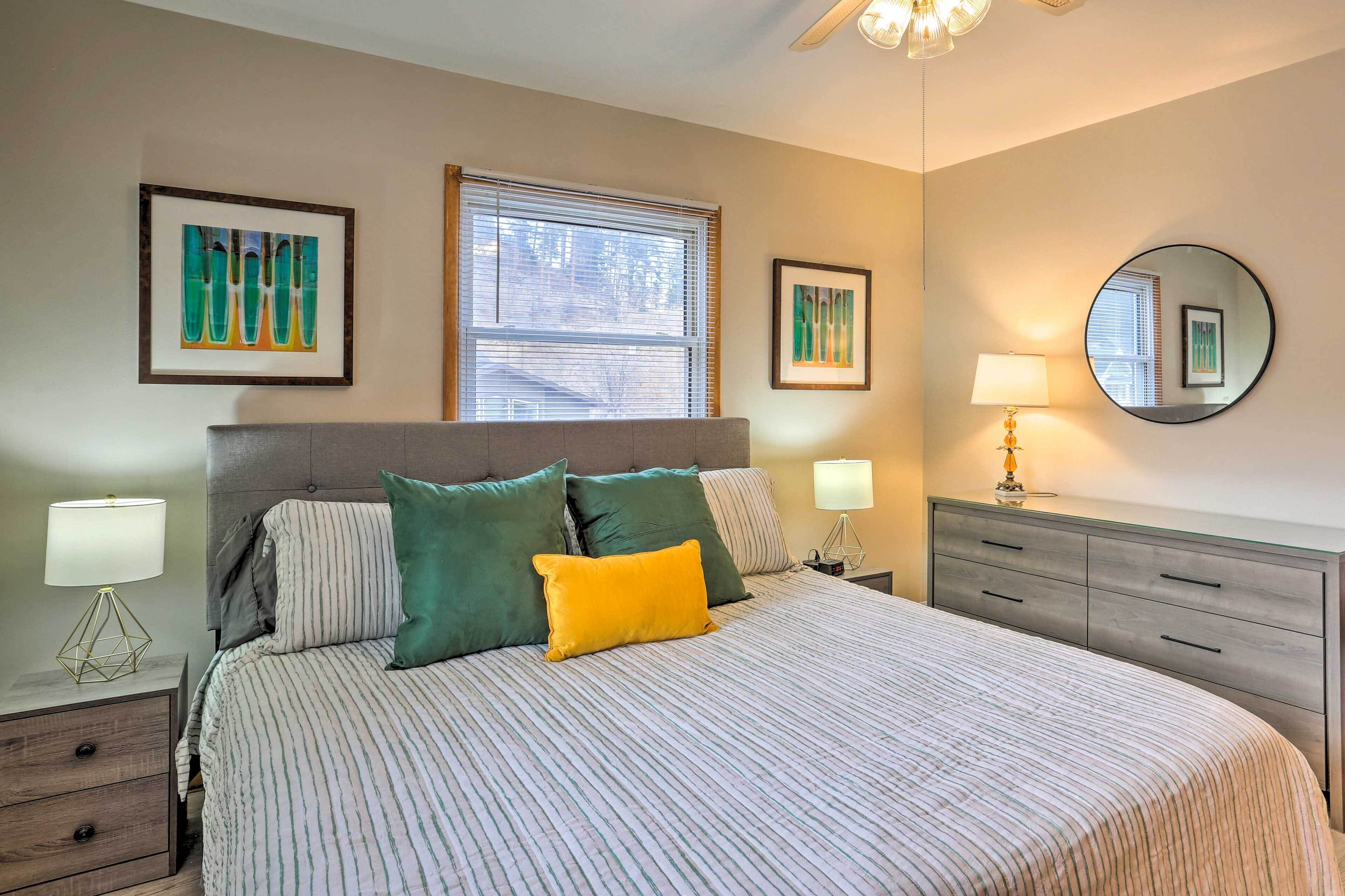 A bedroom with a large bed, two bedside tables with lamps, a dresser, and artwork on the walls.