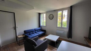 A modern living room with a blue sofa, a black armchair, a small table, and a clock on the wall.