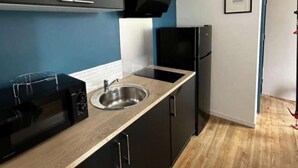 Een kleine keuken met een magnetron, spoelbak en zwarte kastjes.