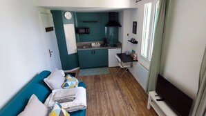 Un espace de vie compact comprenant un coin cuisine, un canapé avec des coussins, un téléviseur et une fenêtre avec des rideaux.