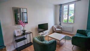 A living room with a TV, two green armchairs, a white coffee table, and a small side table with a picture frame and flowers. - 2-1 Charming T2 bis near train station and town center - Parking nearby (Lourdes)