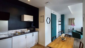 A compact kitchen with white cabinets, a black backsplash, and a teal door. A dining table with chairs is visible in the adjacent room. - 2-1 Charming T2 bis near train station and town center - Parking nearby (Lourdes)