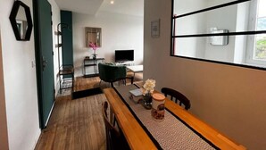 A modern living room with a wooden dining table, a green armchair, and a large window. - 2-1 Charming T2 bis near train station and town center - Parking nearby (Lourdes)