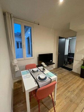 A dining area with a white table set for two, a television, and a view of the outside through a window. - 3-2 T1 Bis Cosy near train station (Lourdes)