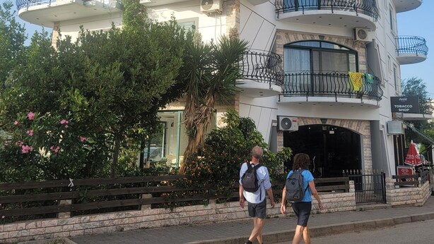 A multi-story building with balconies, a visible shop sign, and a paved entrance area. - Remarkable 4-Bed House in Ksamil for families (Ksamil)
