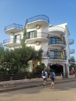A multi-story building with balconies, a visible shop sign, and a paved entrance area. - Remarkable 4-Bed House in Ksamil for families (Ksamil)