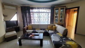 A living room with a sofa, coffee table, TV, and a cabinet with glass doors. - Remarkable 4-Bed House in Ksamil for families (Ksamil)