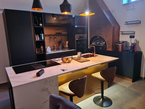 A modern kitchen with a central island, bar stools, pendant lighting, and a built-in oven.