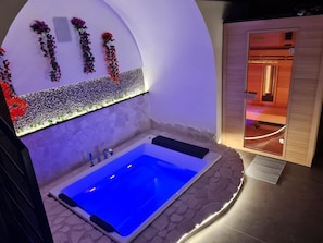 A spa area with a blue-lit hot tub, decorative plants, and a wooden sauna.