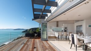 A modern outdoor dining area with a view of the sea, wooden flooring, and contemporary furniture.