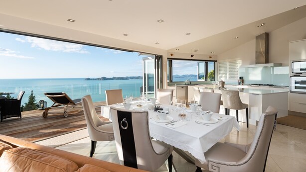 A modern dining area with a table set for four, overlooking a scenic ocean view.